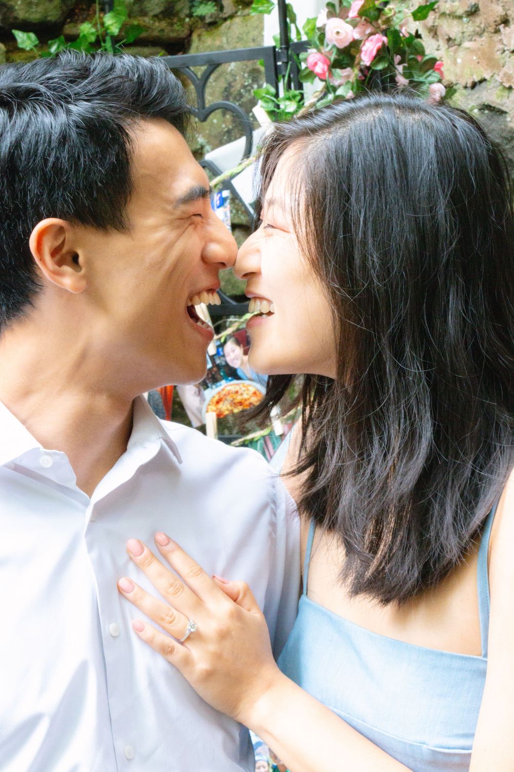 Ecstatic newly engaged couple laughing face to face with engagement ring visible on her hand.