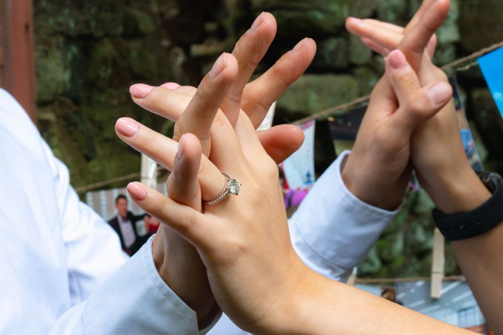 Close-up of hands showing diamond engagement ring with friends celebrating together outdoors.