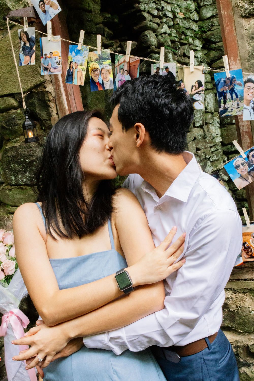 Couple shares romantic kiss during engagement celebration with memory photos displayed behind them.