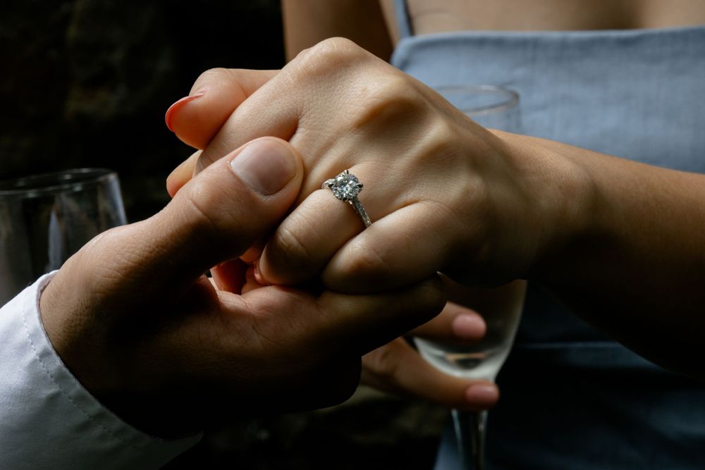 Close-up of engagement ring on bride's hand as couple holds hands with champagne glass.