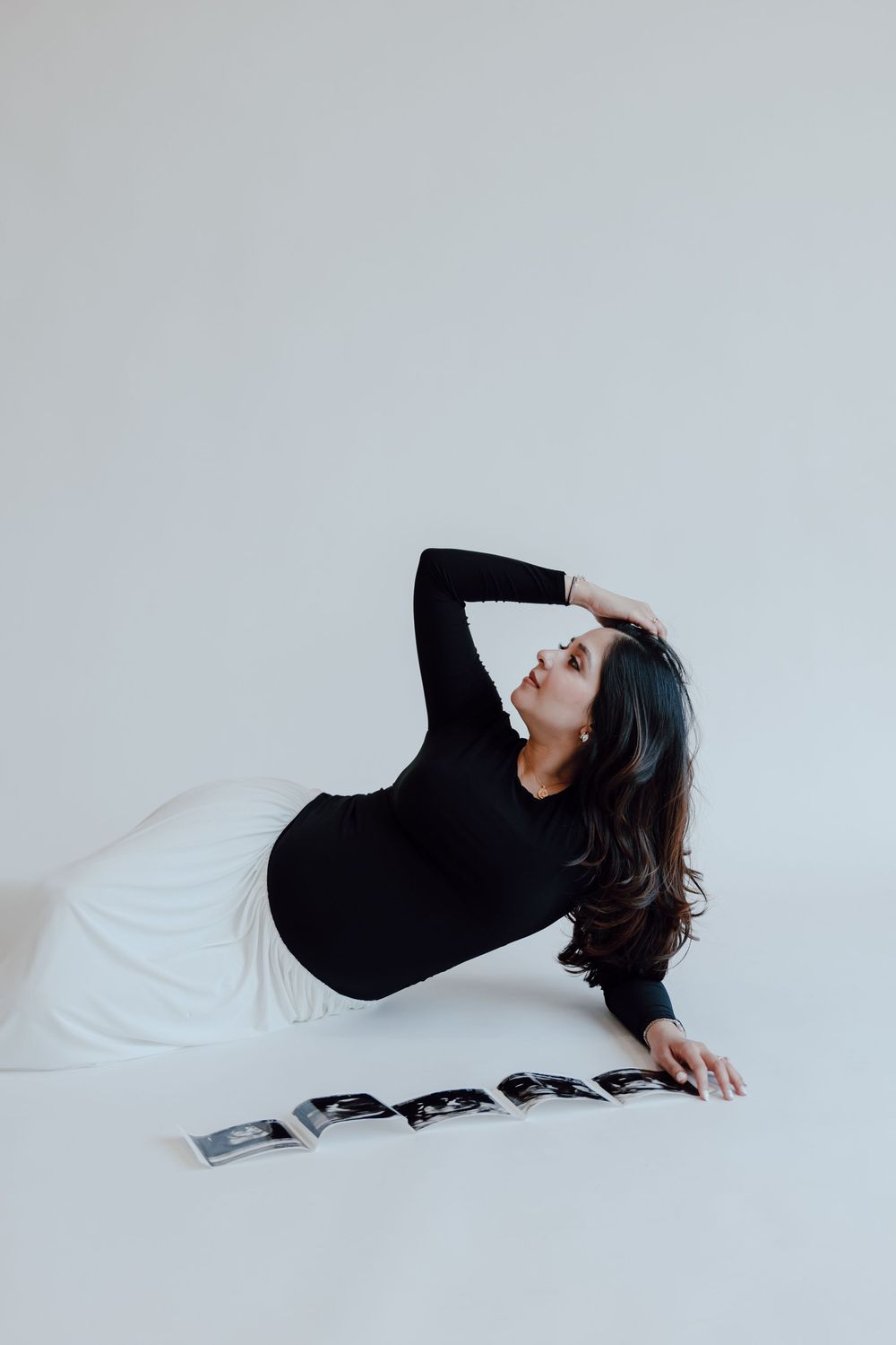 A series of minimalist photos showing a person in black clothing reclining against a white backdrop in artistic poses.