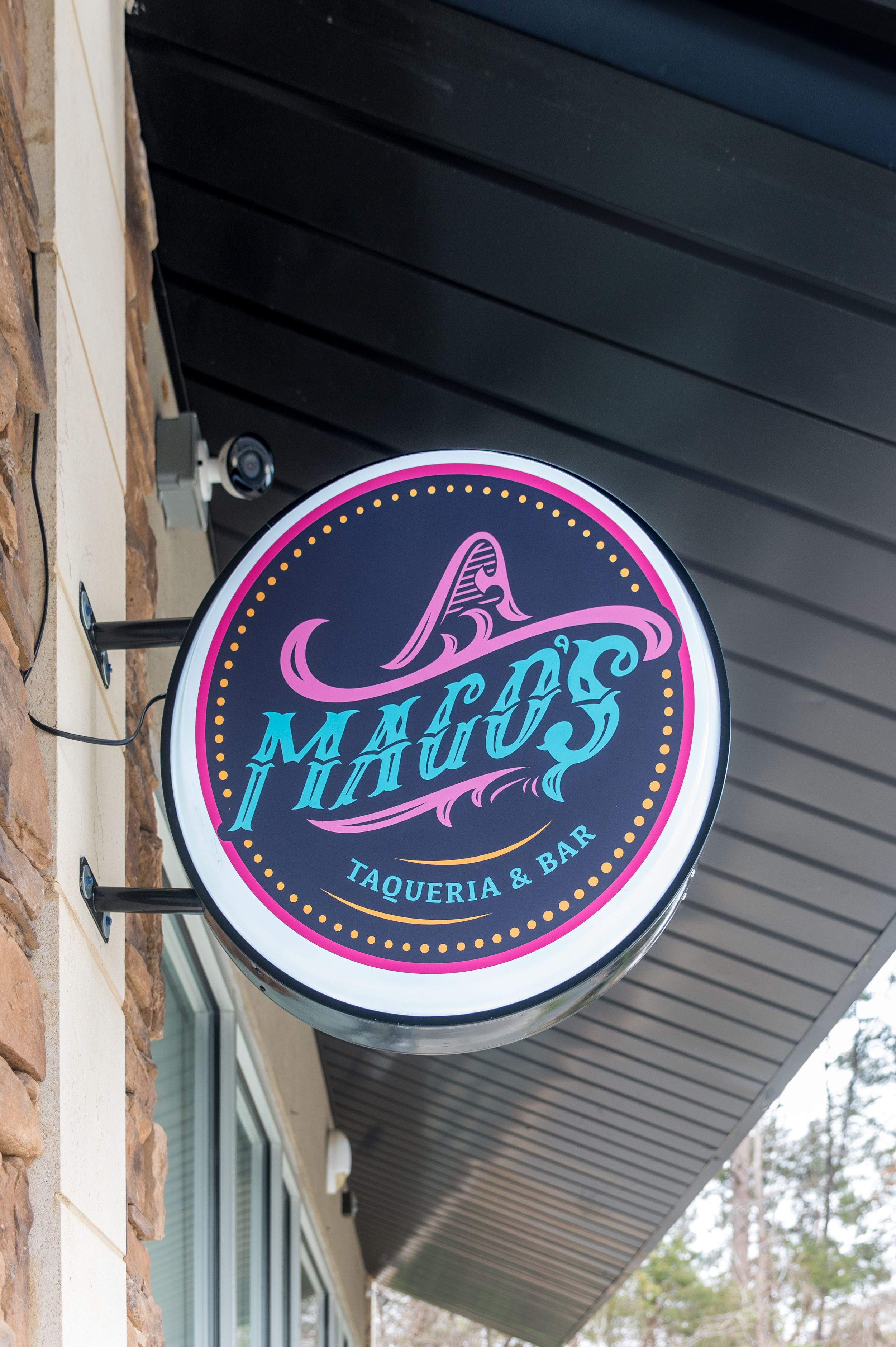 Mago's Taqueria & Bar circular illuminated sign mounted on exterior wall with colorful neon pink and teal lettering.