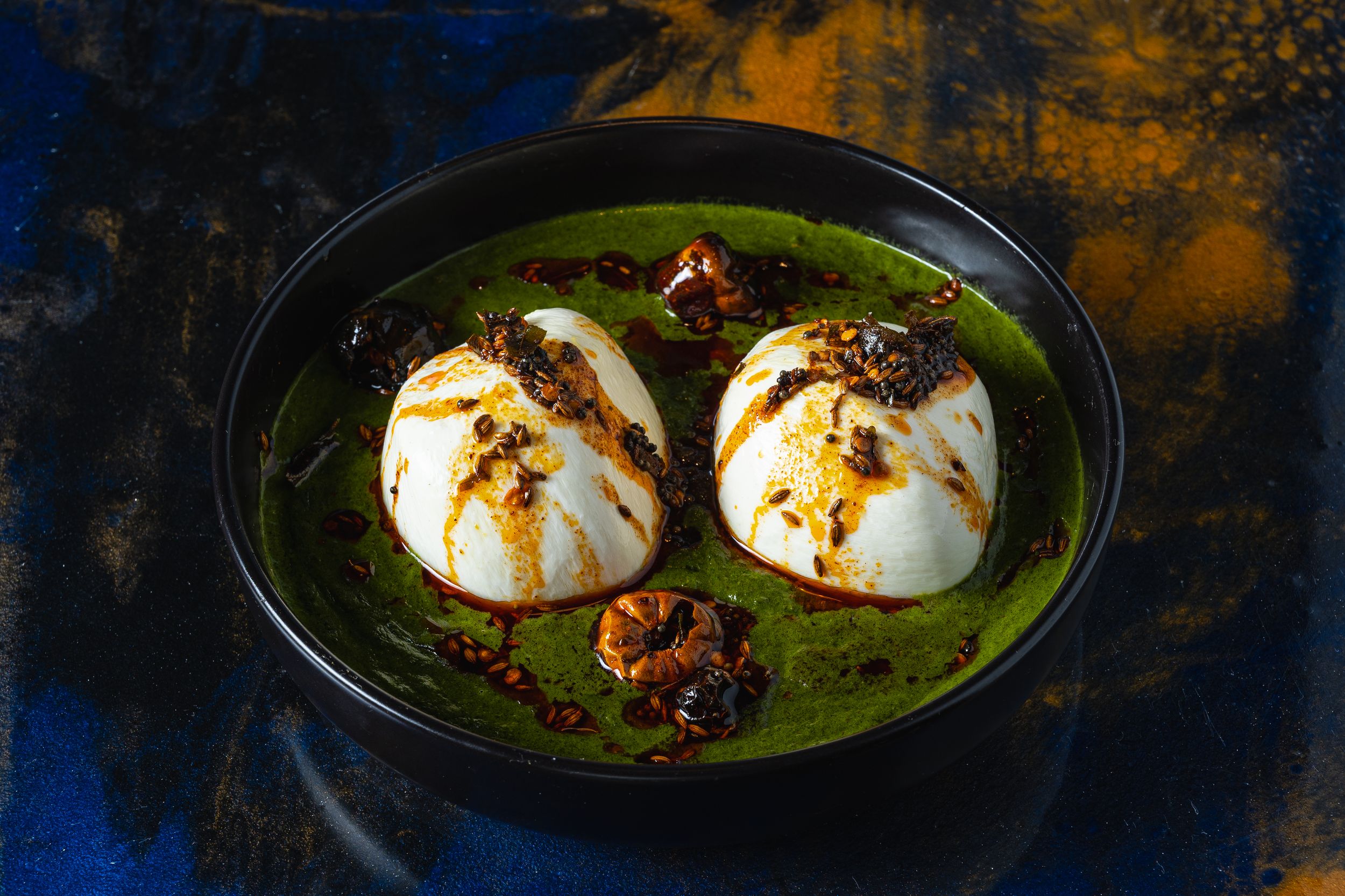 Two poached eggs in vibrant green herb sauce topped with crispy caramelized onions served in a black bowl.