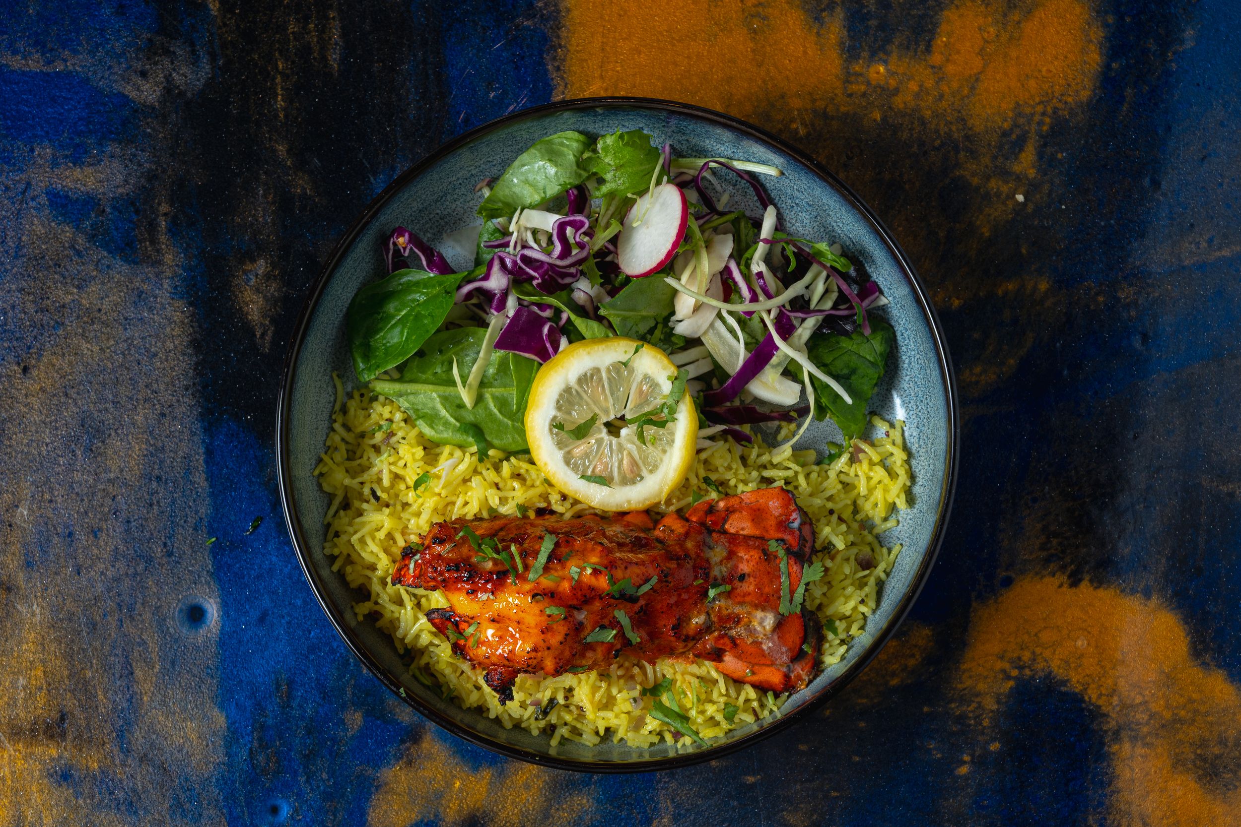 Top-down view of a vibrant salmon rice bowl with turmeric rice, fresh salad, and lemon on a dark plate.