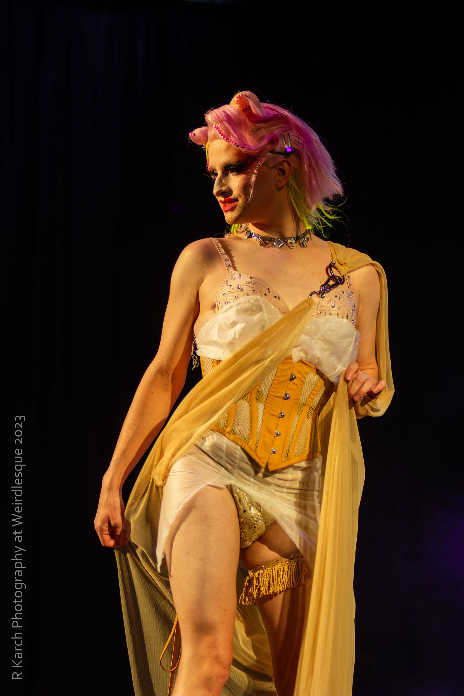 A performer in a vintage-inspired corset and flowing gold fabric on a dark stage.