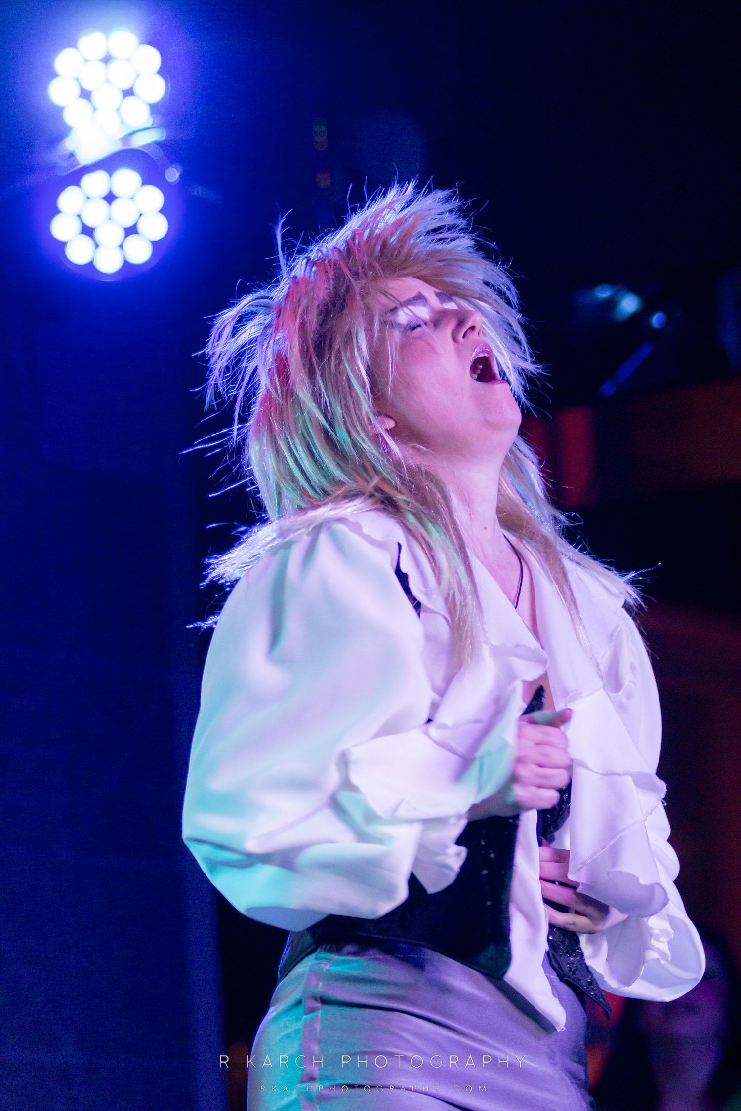 A performer with spiky hair illuminated by blue stage lights during an energetic performance.