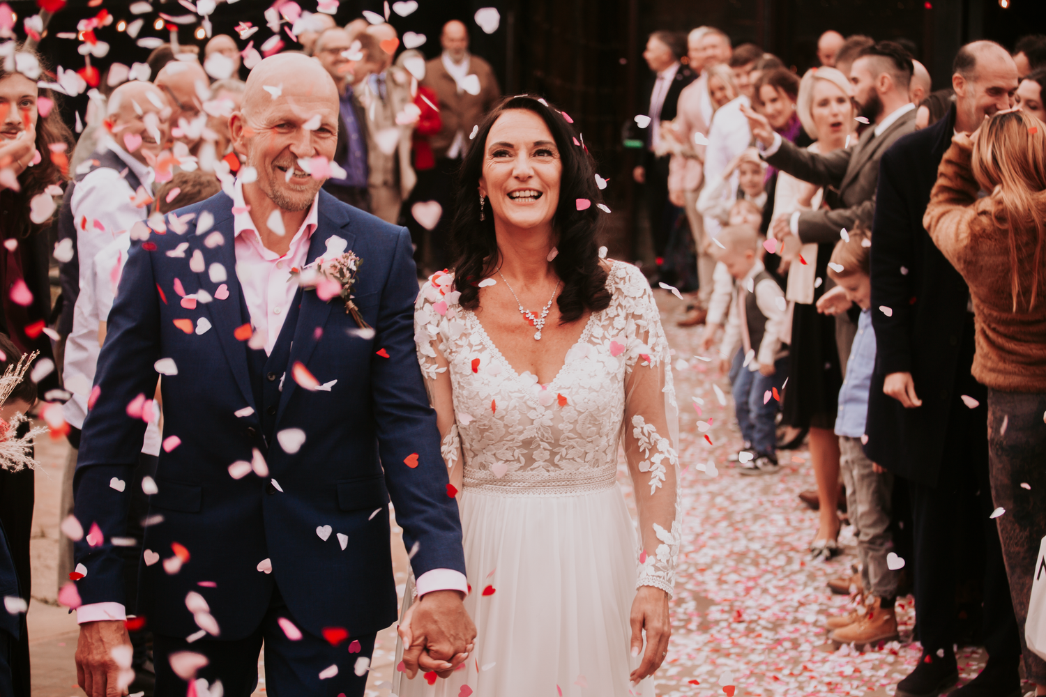Wedding celebration with pink flower petals being thrown in the air during a joyous moment.