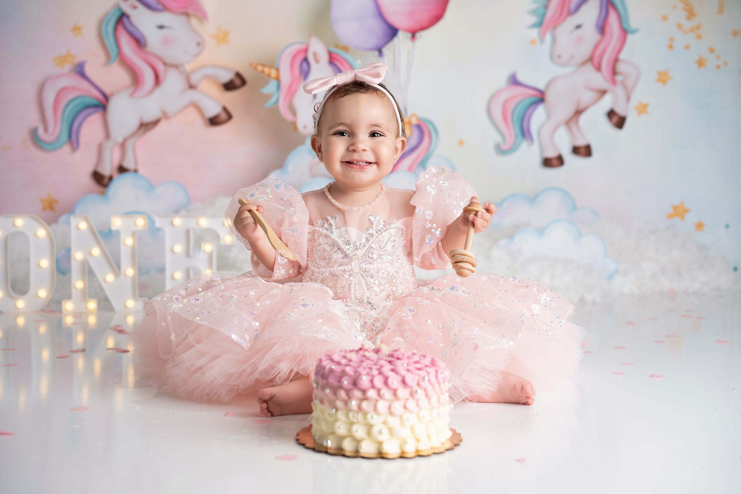 A pink and gold unicorn-themed cake smash photo session featuring a baby in a tulle dress celebrating their first birthday.