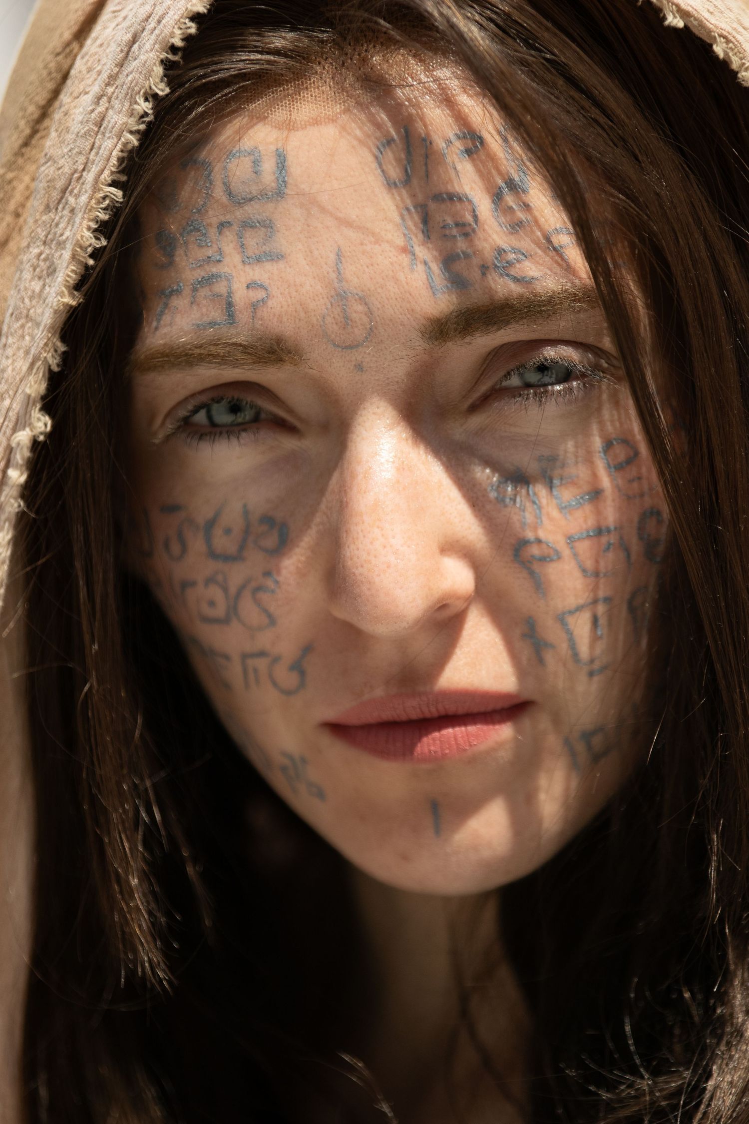 Portrait of person with mystical symbols and writing painted on their face in natural lighting. | Shot By Lo™