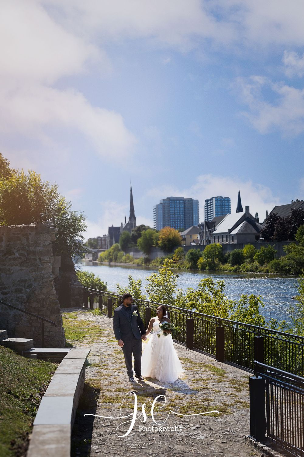 Wedding photography series along waterfront path with city skyline backdrop.