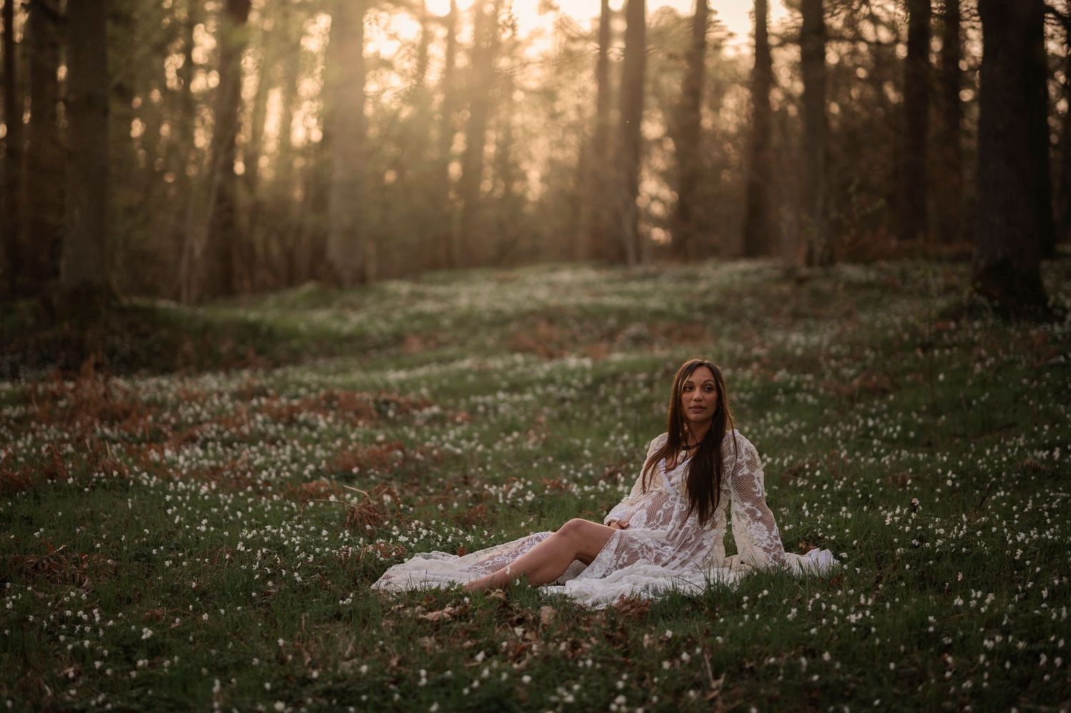 Romantic maternity photo of figure reclining in sunlit meadow wearing white dress.