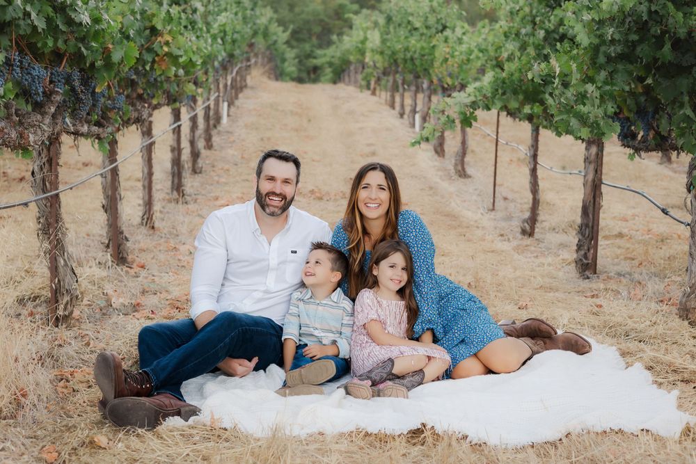 family sitting on blanket in vineyard smiling. Sonoma County California mini session