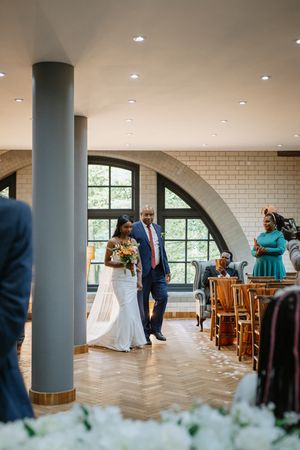 Elegant wedding reception in a modern venue with arched windows, white brick walls, and hardwood herringbone flooring.