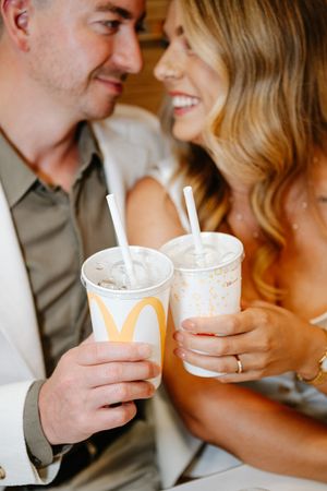 Couple in wedding attire smiling at each other while holding McDonald's drinks with straws.