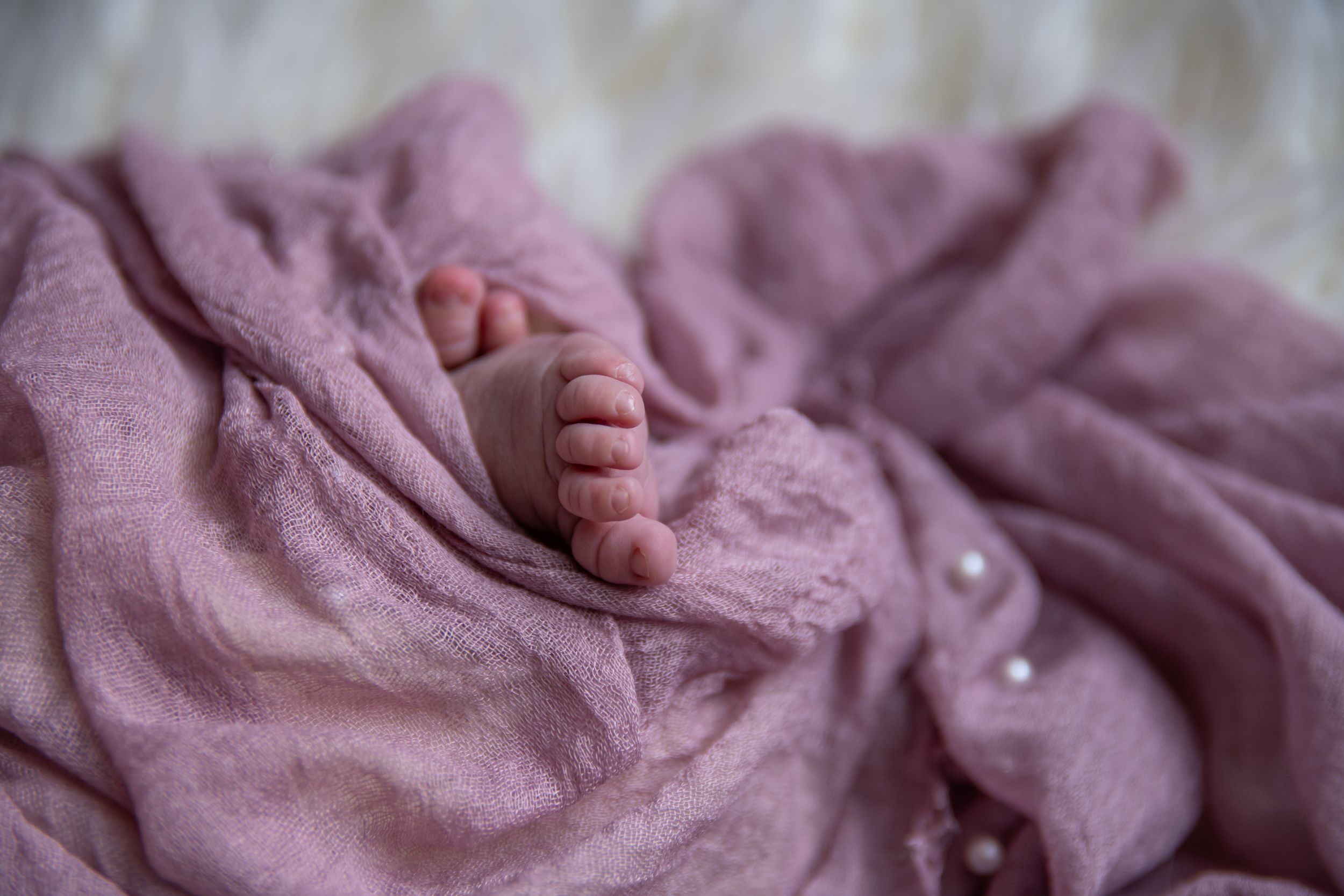 Close up of tiny baby feet resting on soft pink swaddling blanket.