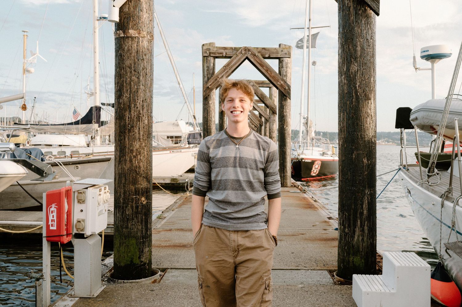 Person in striped sweater standing at marina dock with boats in background.