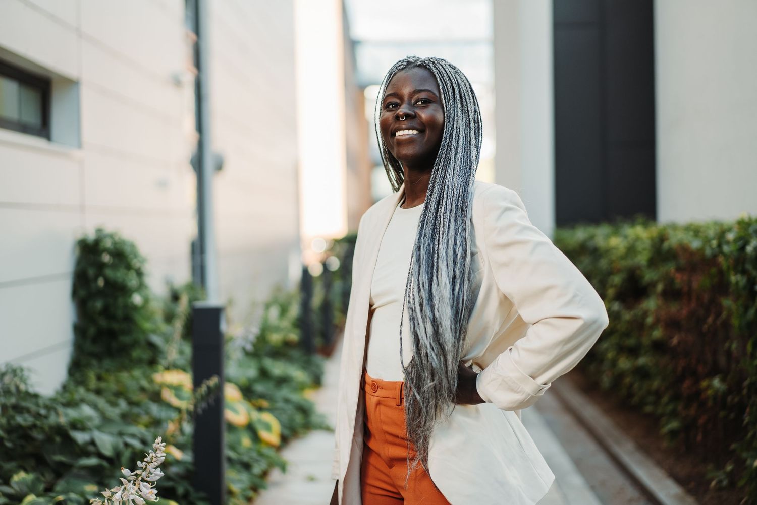 Woman in a white outfit and orange pants smiling outdoors.