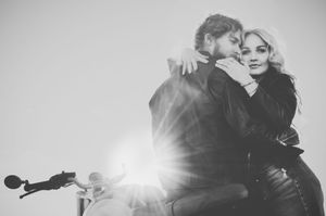 A romantic couple embraces on their motorcycle in a black and white photo while sunlight creates a dreamy backlit effect.
