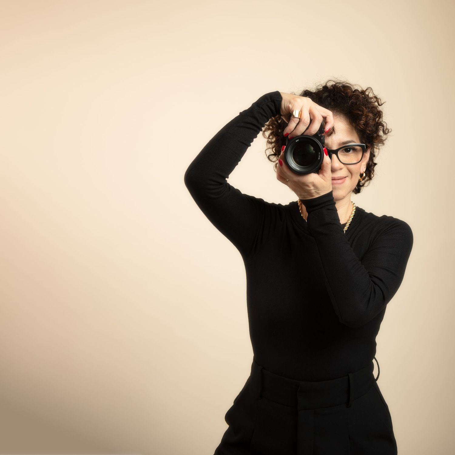 A photographer in black turtleneck and glasses takes photos with professional camera against beige background.