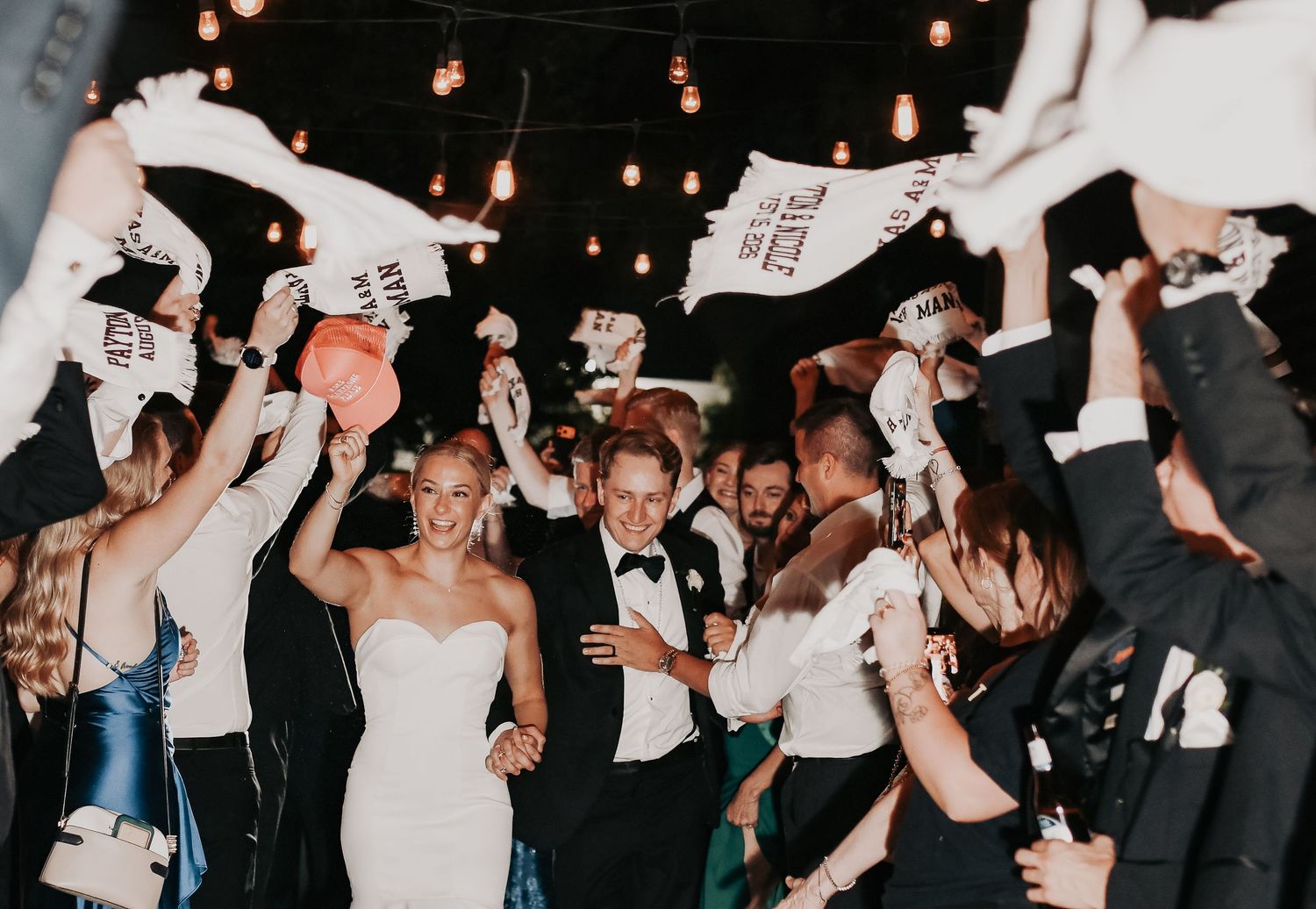 Editorial wedding moment of a bride and groom walking through their reception grand exit as aggie towels wave