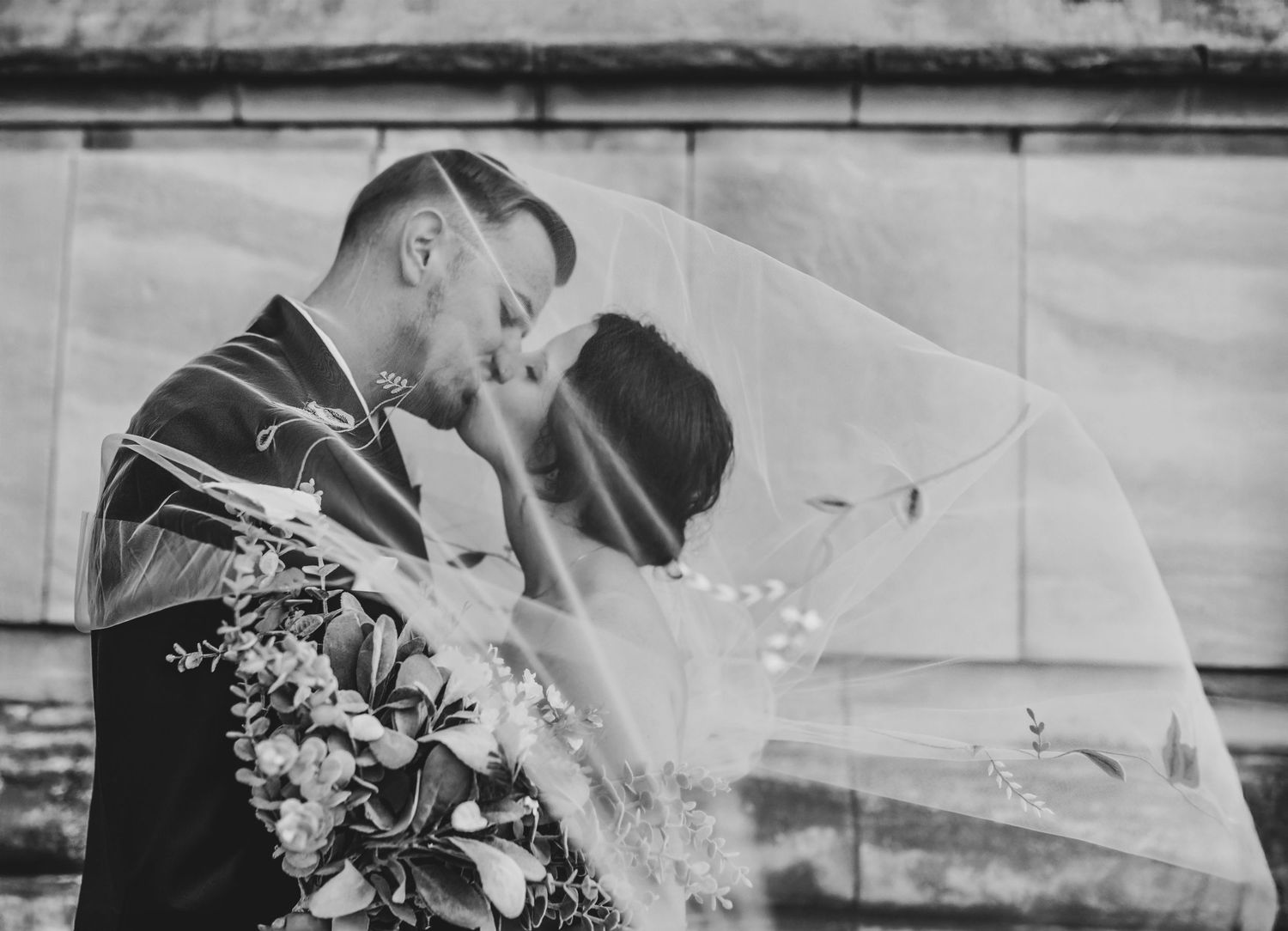 Editorial wedding moment of a couple kissing beneath the brides flowing veil