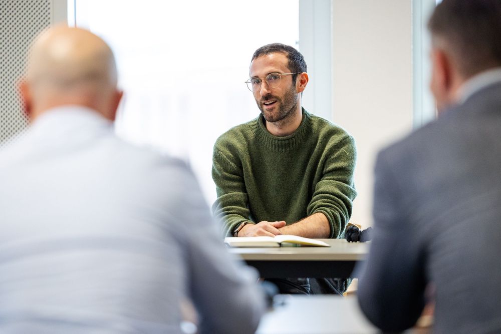 A man in a green sweater speaks during a small group discussion at a business event.