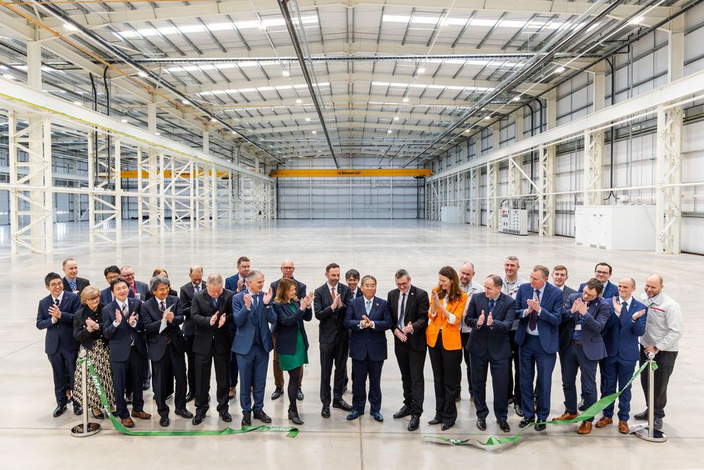 Ribbon-cutting ceremony with a large group of officials celebrating inside a spacious newly completed industrial facility.