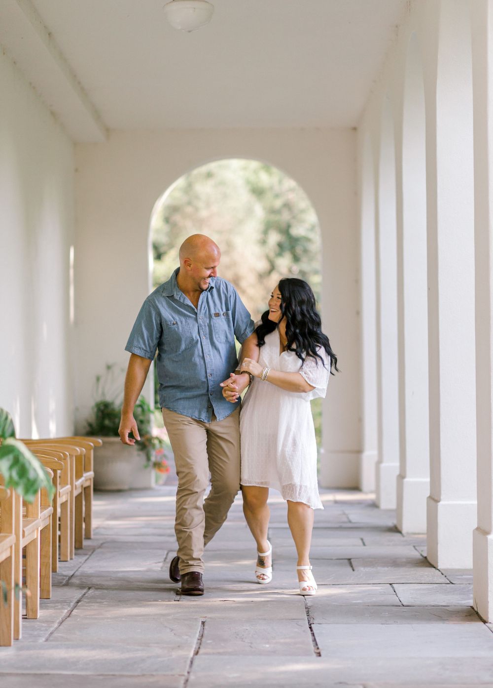 Couple walking hand in hand through elegant white columned corridor, man in blue shirt and woman in white dress. Newfields. Indiana.
