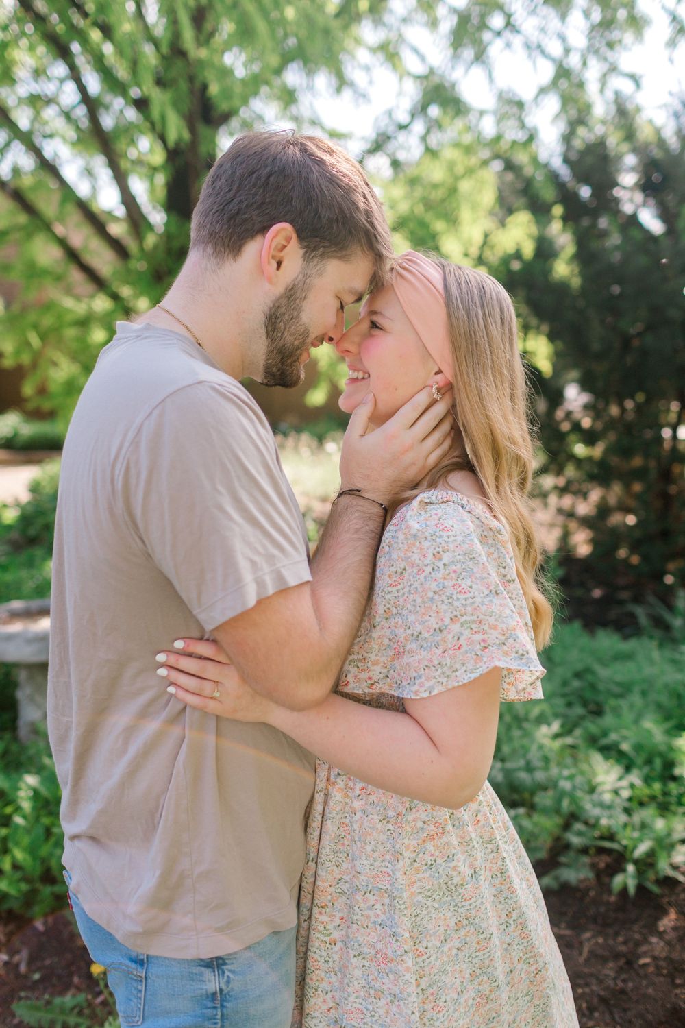 Couple almost kissing in a sun-dappled garden, man gently cradling womans face in his hands.
