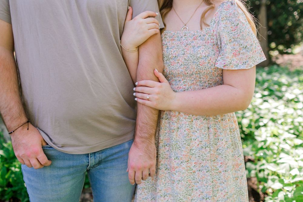 Close-up of couple holding hands, woman in floral dress gently touching mans arm outdoors.