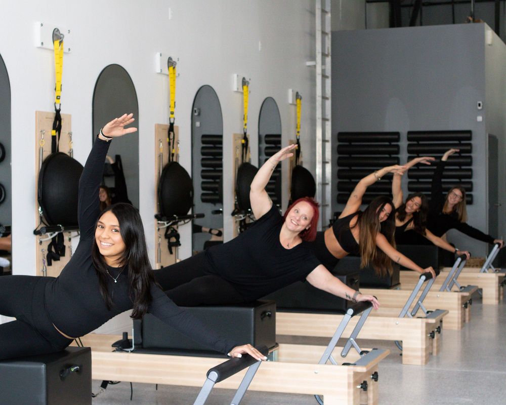 Group workout session in pilates studio showing various reformer exercises.