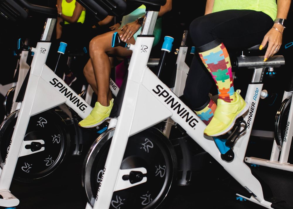 Legs wearing colorful socks pedaling on white spinning exercise bikes at a gym class.