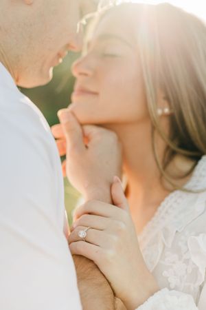 Couple sharing a romantic moment in golden sunlight, woman wearing a diamond engagement ring on her hand.