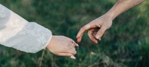 Two people gently touching fingertips outdoors, symbolizing connection and love against a green grass background.