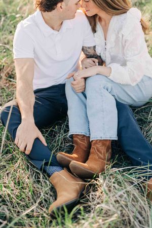 Couple sitting in grass wearing jeans and cowboy boots, sharing a romantic moment outdoors in natural light.