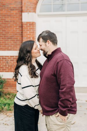 Couple in casual sweaters share a tender moment while standing against a brick building downtown Lawrenceville Courthouse