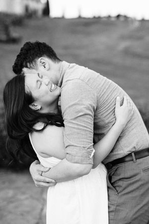 Black and white photo of couple laughing and embracing outdoors during romantic engagement session.