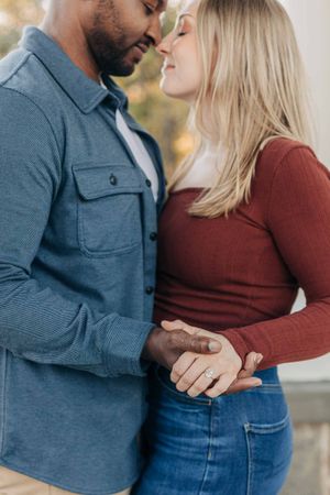 Interracial couple holding hands and sharing a romantic moment, woman wearing engagement ring.
