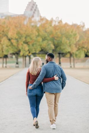 Interracial couple walking arm in arm along a path surrounded by colorful autumn trees.