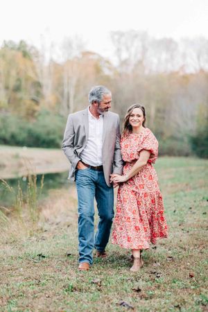 A couple walks together through an autumn field wearing coordinated casual outfits in Monroe Georgia.