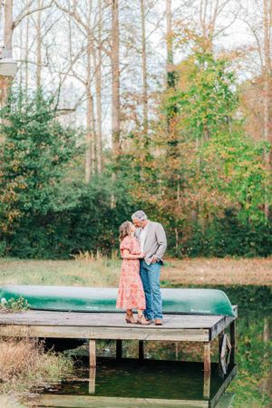 A romantic couple stands together on a wooden dock surrounded by autumn trees in Monroe Georgia.