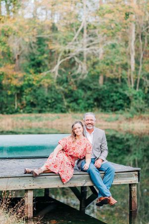 A couple sits together on a wooden dock overlooking a scenic autumn landscape in Monroe Georgia