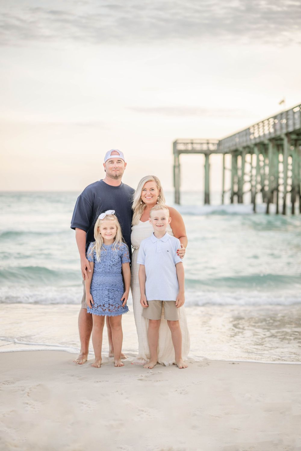 A family poses together on a beach at sunset with a wooden pier in the background.