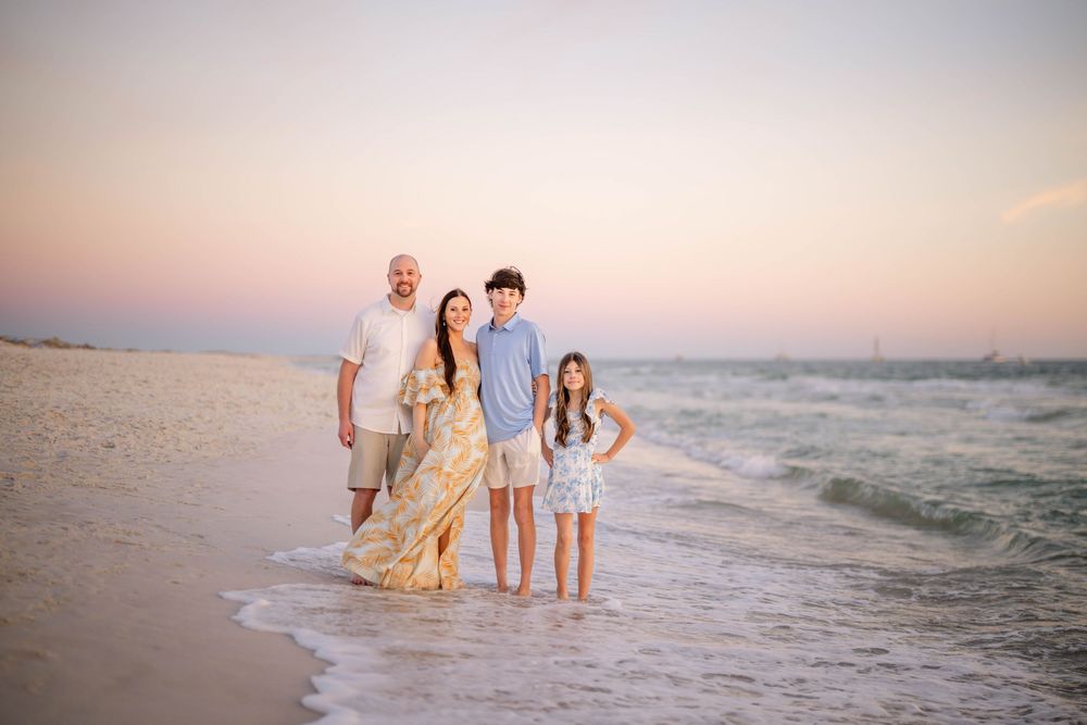 A group stands together at the beach during sunset while gentle waves lap at their feet on the sandy shore.