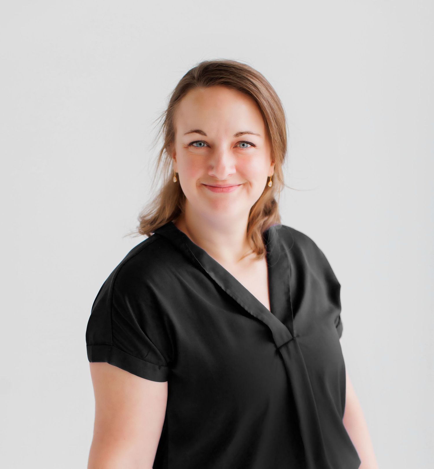 Professional woman in black top smiling confidently against a light gray background.