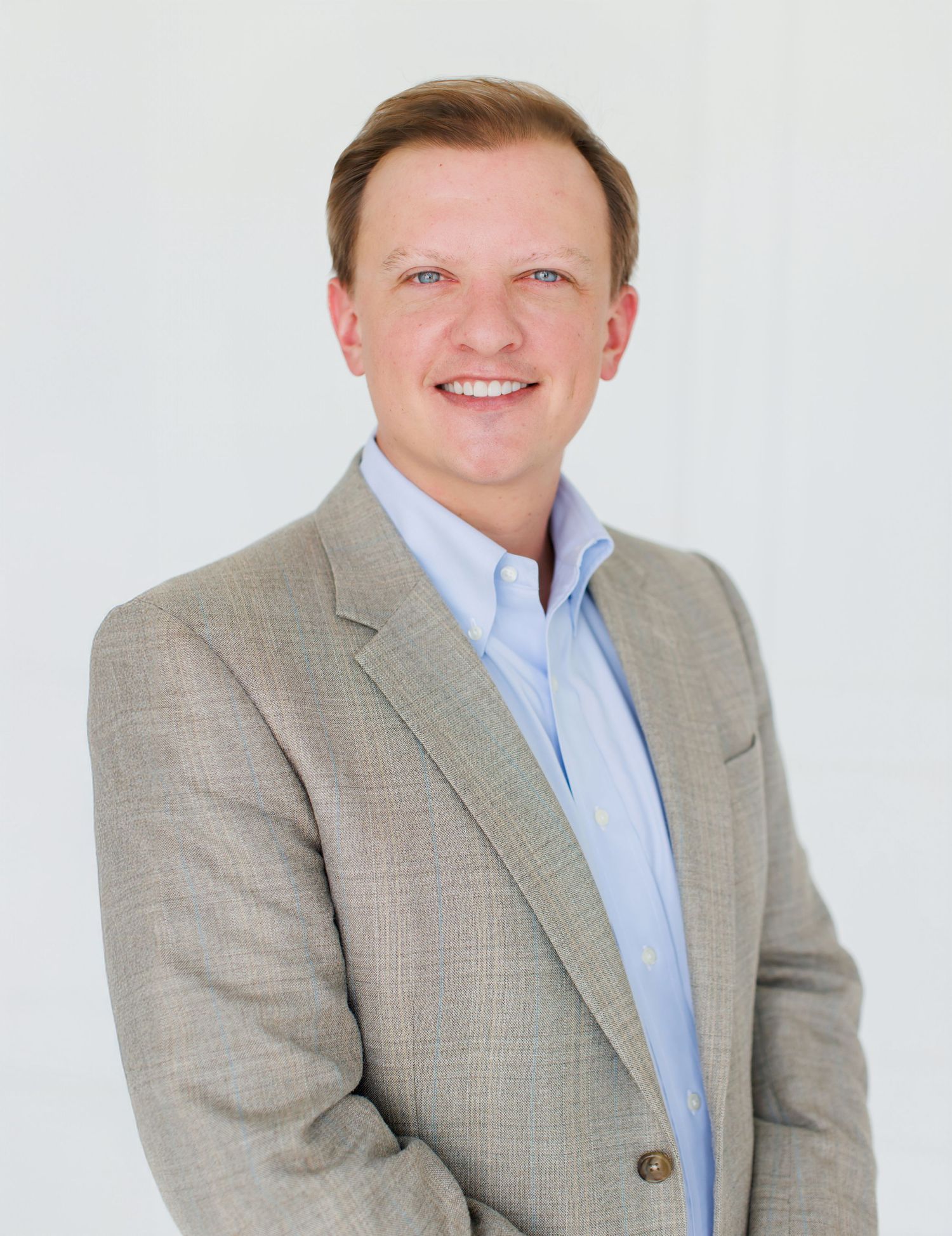Professional headshot of a smiling man in a light gray blazer and blue shirt against a white background.