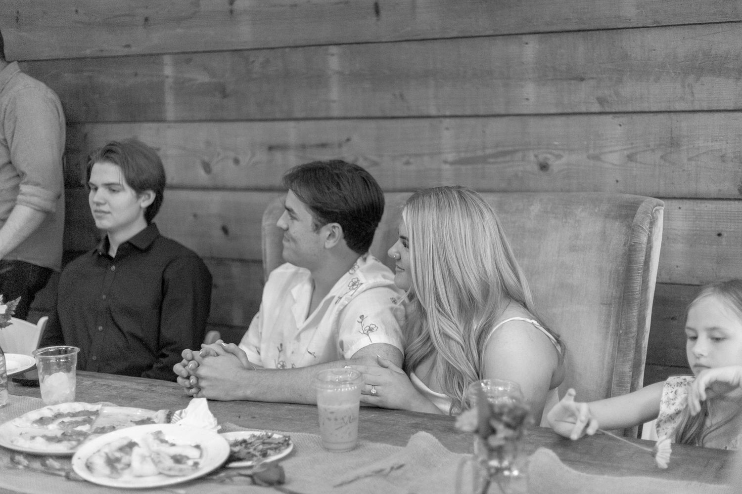 Black and white photo of guests seated at an outdoor wooden table enjoying a meal together.