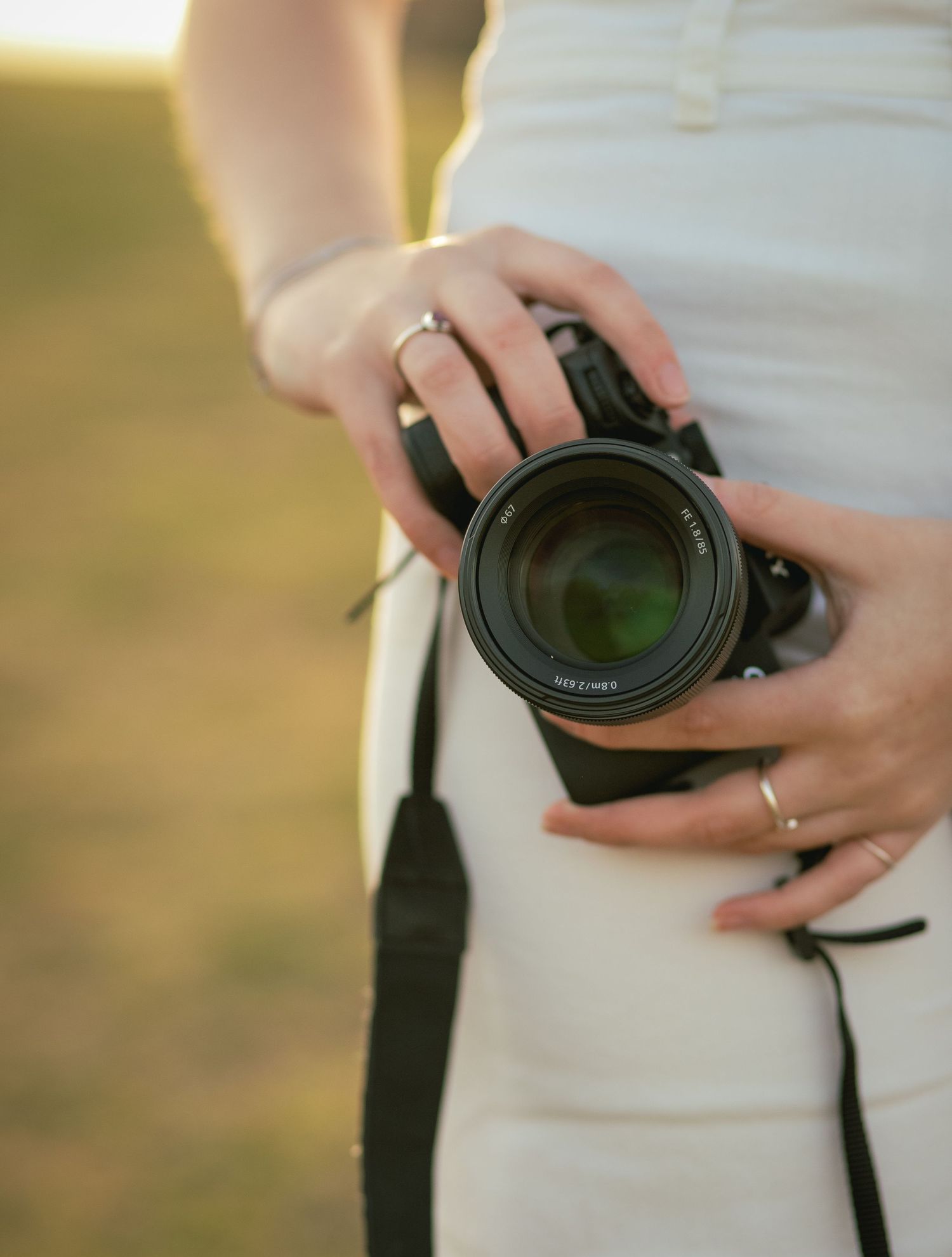 Close-up of woman's hands holding a DSLR camera with a large lens outdoors at golden hour.