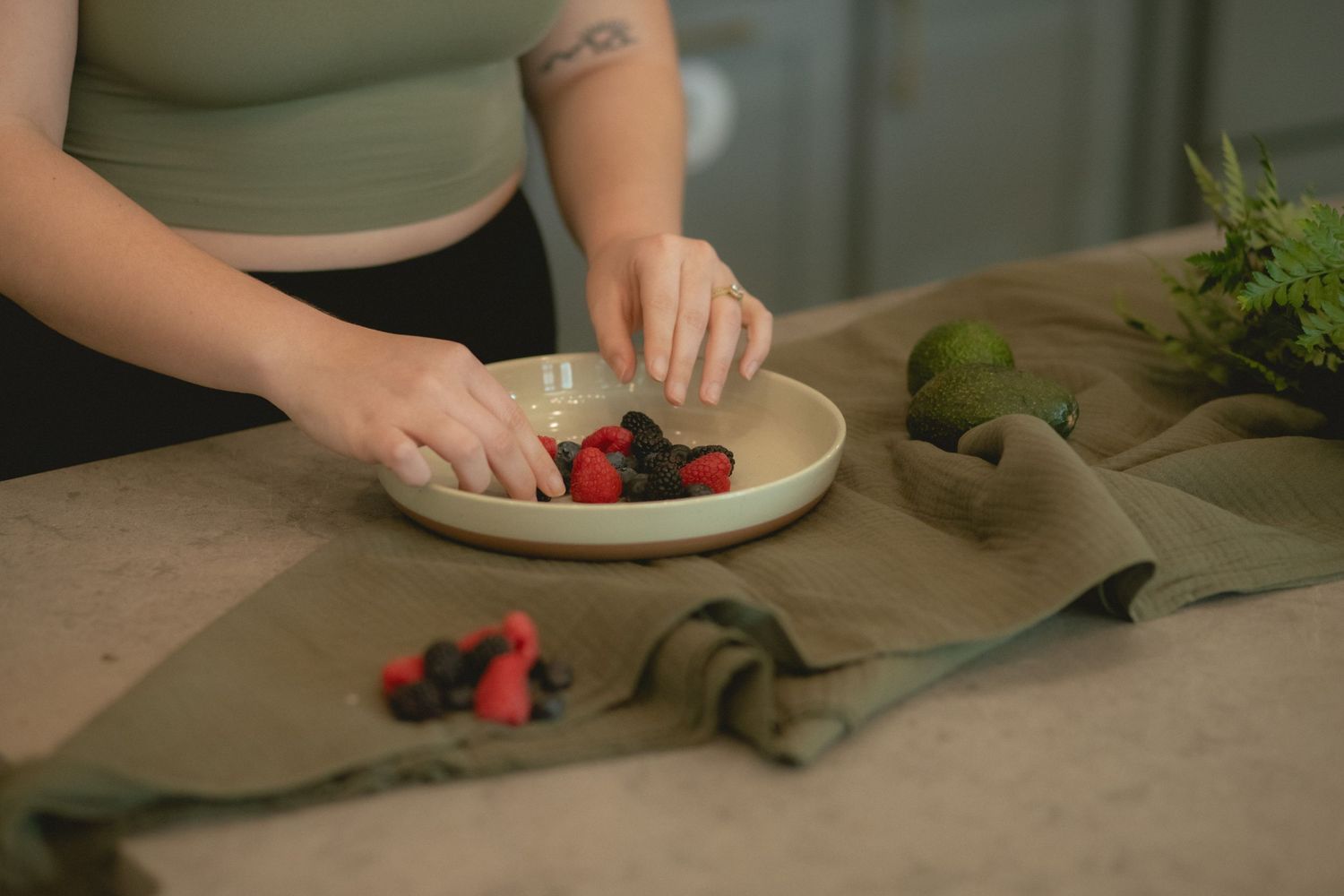 Close-up of hands arranging fresh mixed berries in a ceramic bowl on a kitchen counter.