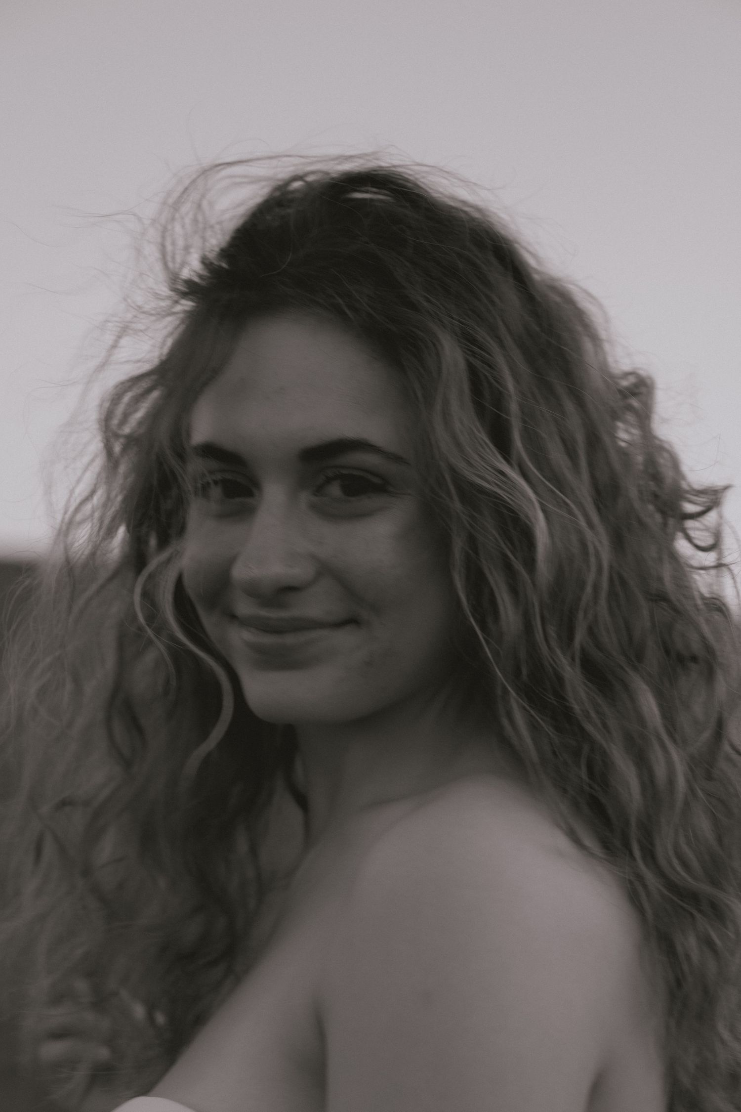 Black and white close-up portrait of a young woman with long curly hair smiling softly.